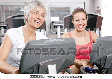 portrait of two woman on stationary bicycles in gym View Large Photo Image Stock Image - portrait of two woman on stationary bicycles in gym. Fotosearch