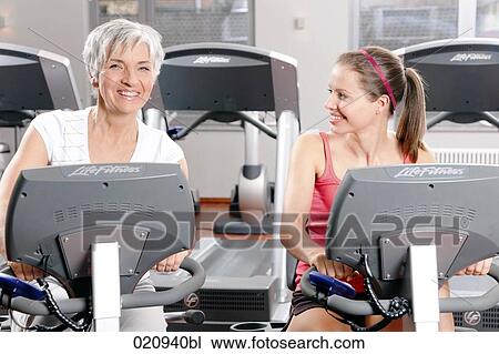 Stock Image - portrait of two woman on stationary bicycles in gym. Fotosearch