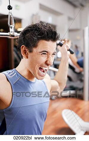 Stock Image - portrait of young man exercising with weight machine. Fotosearch