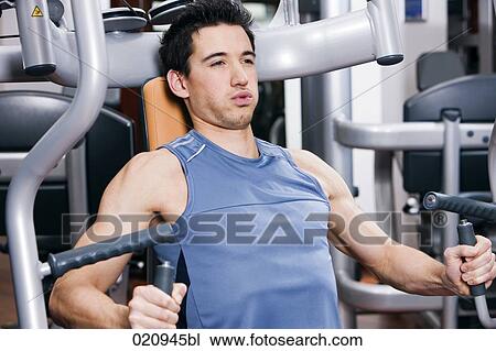 Stock Image - portrait of young man exercising with weight machine. Fotosearch