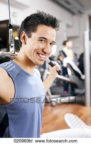 Stock Image - portrait of young man exercising with weight machine. Fotosearch