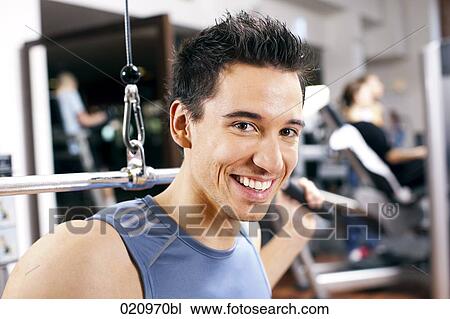 Stock Image - portrait of young man exercising with weight machine. Fotosearch