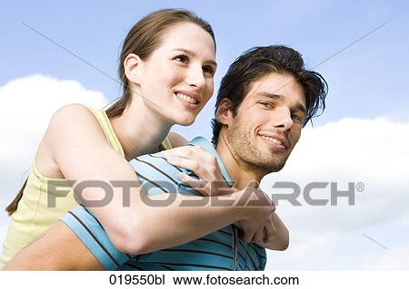 Stock Image - portrait of young man giving girlfriend piggyback ride. Fotosearch
