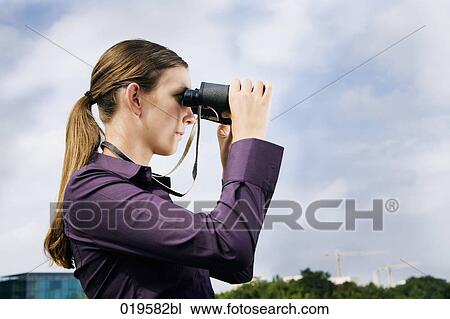 Stock Image - side view of young businesswoman looking through binoculars. Fotosearch