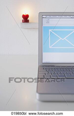 Stock Image - still life of laptop computer with heart shaped candle burning in background. Fotosearch