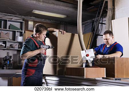 Stock Image - two craftsmen assembling furniture in workshop. Fotosearch