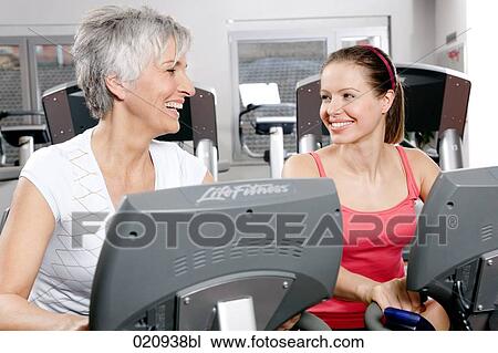two women on stationary bicycles in gym smiling at each other View Large Photo Image Stock Image - two women on stationary bicycles in gym smiling at each other. Fotosearch