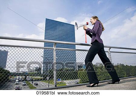 Stock Image - young businesswoman standing on bridge shouting through megaphone. Fotosearch