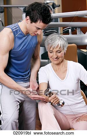 young man showing mature woman how to exercise with dumb bell View Large Photo Image Stock Image - young man showing mature woman how to exercise with dumb bell. Fotosearch