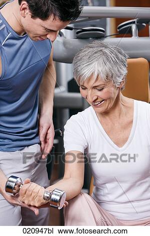 young man showing mature woman how to exercise with dumb bell View Large Photo Image Stock Image - young man showing mature woman how to exercise with dumb bell. Fotosearch