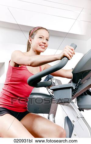Stock Image - young woman exercising with stationary bicyle in gym. Fotosearch