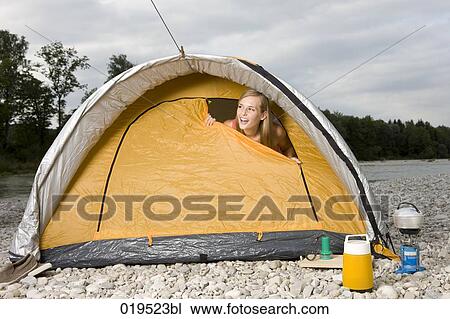 Stock Image - young woman peeking through tent in the morning. Fotosearch