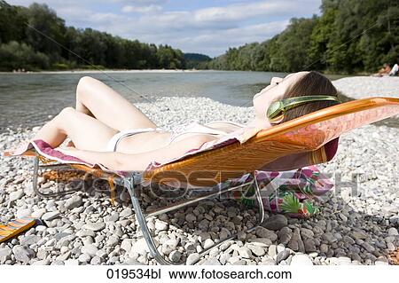 young woman taking sunbath by river listening to music View Large Photo Image Stock Image - young woman taking sunbath by river listening to music. Fotosearch