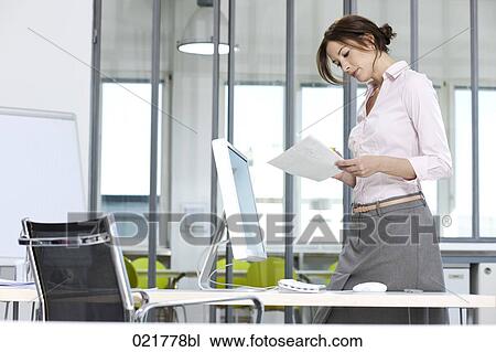 Stock Image - businesswoman standing in office reading document. Fotosearch