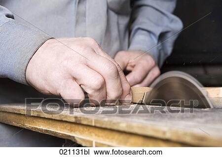Stock Image - close-up of carpenter cutting piece of wood with buzz saw. Fotosearch