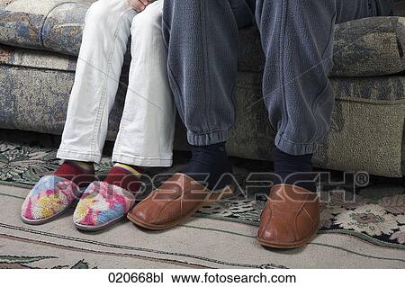Stock Image - detail of mature couple sitting on sofa wearing slippers. Fotosearch