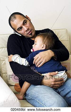 father sitting on sofa and holding his sleeping son while talking on mobile phone View Large Photo Image Stock Image - father sitting on sofa and holding his sleeping son while talking on mobile phone. Fotosearch