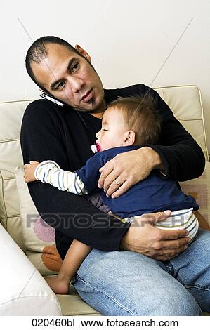 father sitting on sofa and holding his sleeping son while talking on mobile phone View Large Photo Image Stock Image - father sitting on sofa and holding his sleeping son while talking on mobile phone. Fotosearch