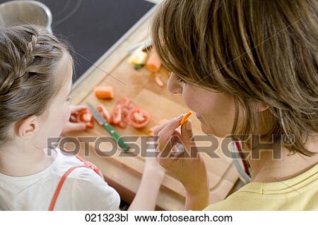 Stock Image - mother and daughter in kitchen mother tasting carrot. Fotosearch