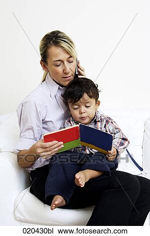mother sitting on sofa talking on mobile phone and reading book to little son View Large Photo Image Stock Image - mother sitting on sofa talking on mobile phone and reading book to little son. Fotosearch
