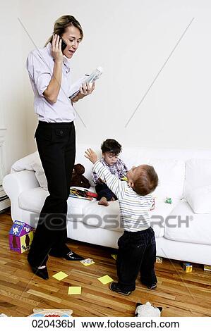 Stock Image - mother sitting on sofa talking on mobile phone while children are playing. Fotosearch