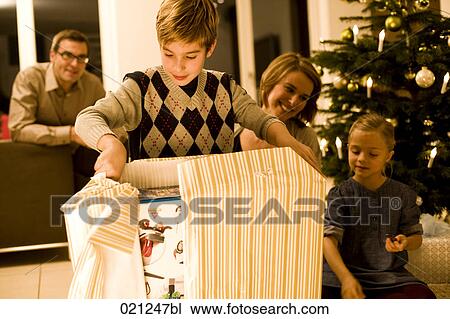 Stock Image - parents watching their children opening christmas presents on christmas eve. Fotosearch