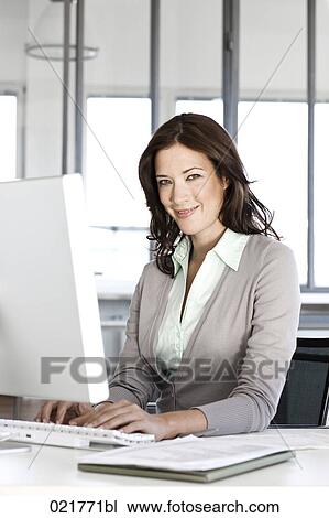 portrait of businesswoman sitting at desk working with computer View Large Photo Image Stock Image - portrait of businesswoman sitting at desk working with computer. Fotosearch