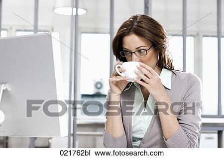 Stock Image - portrait of businesswoman sitting in front of computer drinking coffee. Fotosearch