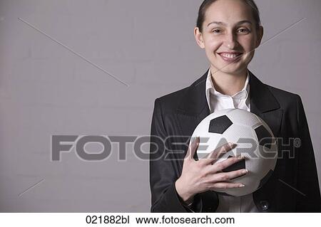 Stock Image - portrait of young businesswoman holding football. Fotosearch