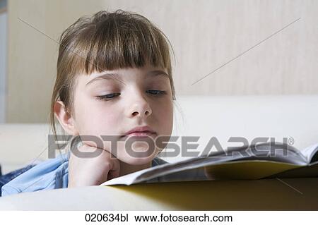 Stock Image - portrait of young girl on sofa reading book. Fotosearch