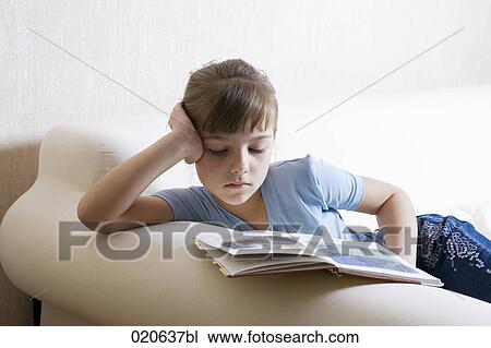 Stock Image - portrait of young girl on sofa reading book. Fotosearch