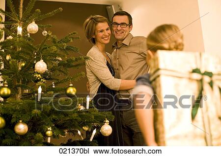 smiling parents looking at daughter holding christmas present behind her back View Large Photo Image Stock Image - smiling parents looking at daughter holding christmas present behind her back. Fotosearch
