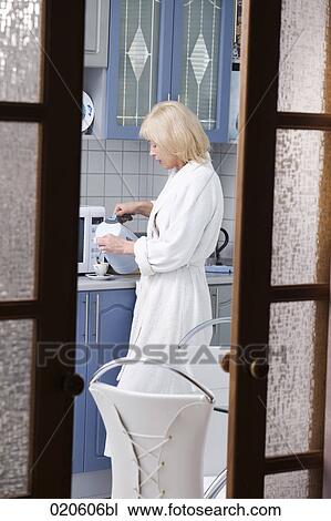view into kitchen with woman in bathrobe pouring coffee into cup View Large Photo Image Stock Image - view into kitchen with woman in bathrobe pouring coffee into cup. Fotosearch