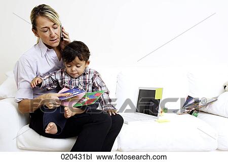 Stock Image - woman sitting on sofa with little son on lap and talking on mobile phone. Fotosearch
