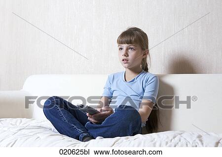 Stock Image - young girl sitting on sofa watching television. Fotosearch
