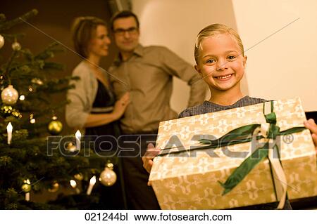 young girl with christmas present parents watching in the background View Large Photo Image Stock Image - young girl with christmas present parents watching in the background. Fotosearch