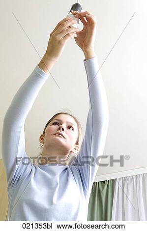 Stock Image - young woman fixing low energy light bulb. Fotosearch