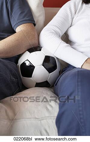 Stock Image - detail of coupe sitting on sofa with football between them. Fotosearch