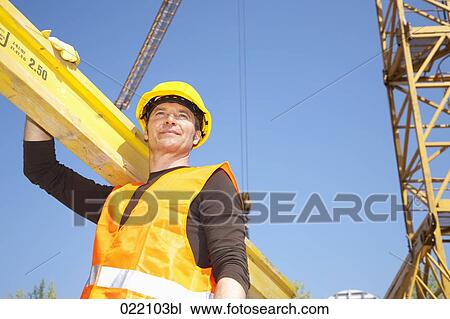 Stock Image - low angle portrait of construction worker carrying wooden plank. Fotosearch
