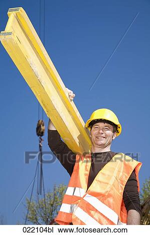 Stock Image - low angle portrait of construction worker carrying wooden plank. Fotosearch