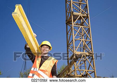 Stock Image - low angle portrait of construction worker carrying wooden plank. Fotosearch