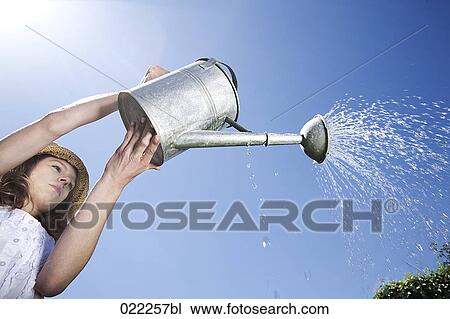low angle view of young woman pouring water from watering can View Large Photo Image Stock Image - low angle view of young woman pouring water from watering can. Fotosearch