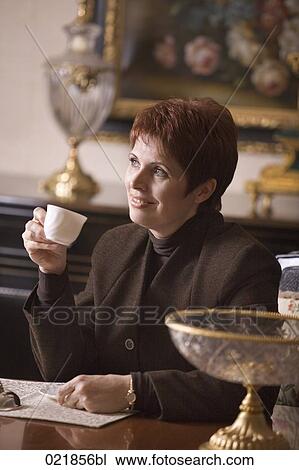 Stock Image - mature woman sitting in living room drinking coffee. Fotosearch