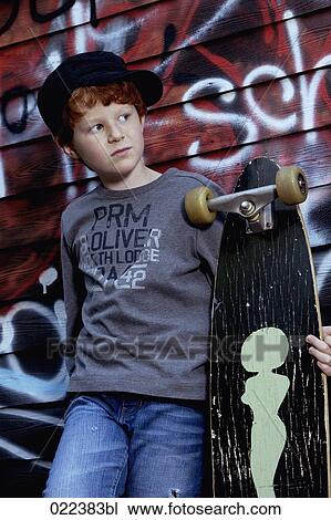 Stock Image - portrait of red haired boy with skateboard leaning against wall. Fotosearch