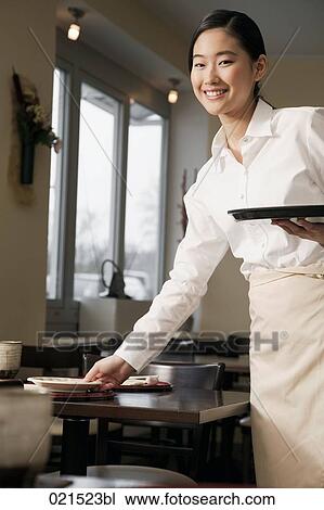 Stock Image - portrait of young japanese waitress setting table at restaurant. Fotosearch