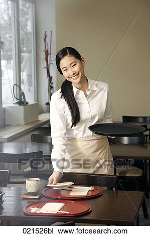 Stock Image - portrait of young japanese waitress setting table at restaurant. Fotosearch