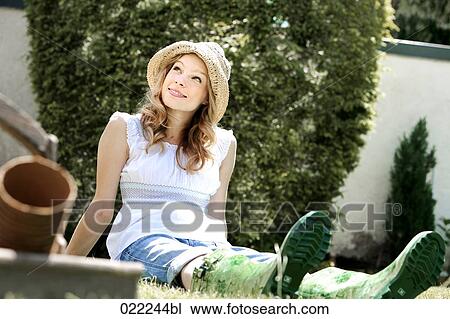 Stock Image - portrait of young woman in garden wearing straw hat. Fotosearch