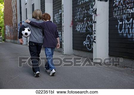 rear view of two young boys walking together through street with football View Large Photo Image Stock Image - rear view of two young boys walking together through street with football. Fotosearch