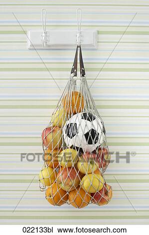 Stock Image - still life of fruit and football in string bag on coat hook. Fotosearch