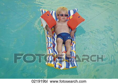 Stock Image - young boy lying on air bed floating in swimming pool. Fotosearch